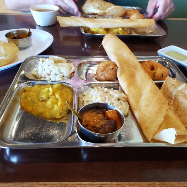 A metal tray with various Indian dishes, including dosa, curries, and rice, on a wooden table.