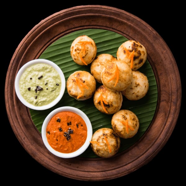 Indian paniyaram with two chutneys on a banana leaf-lined wooden plate.