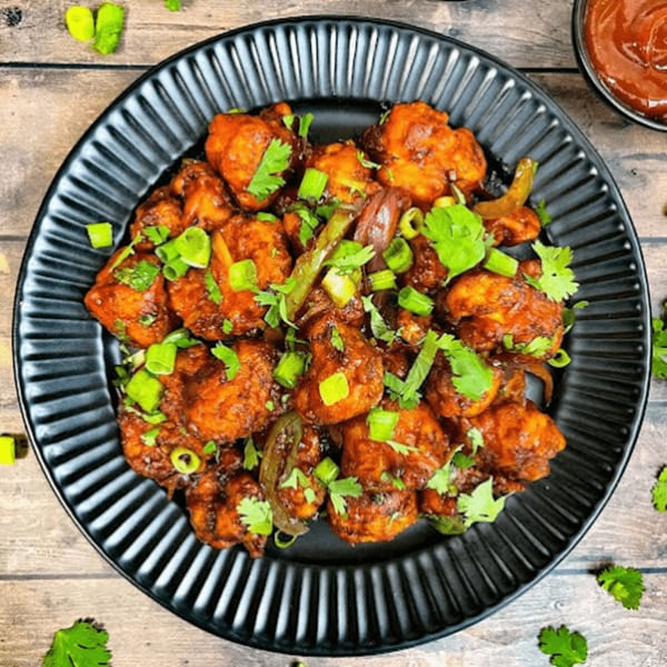 Spicy Indian Gobi Manchurian, a fried cauliflower dish, garnished with green onions and cilantro on a black plate.