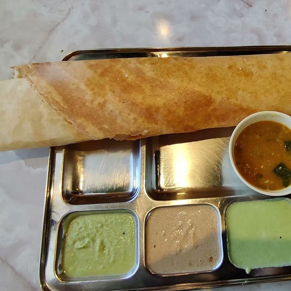 A golden-brown dosa with three chutneys and sambar in a steel thali from Chennai Dosa Hut.