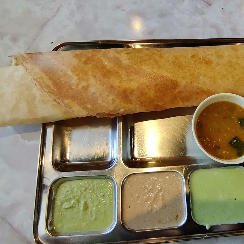 A golden-brown dosa with three chutneys and sambar in a steel thali from Chennai Dosa Hut.